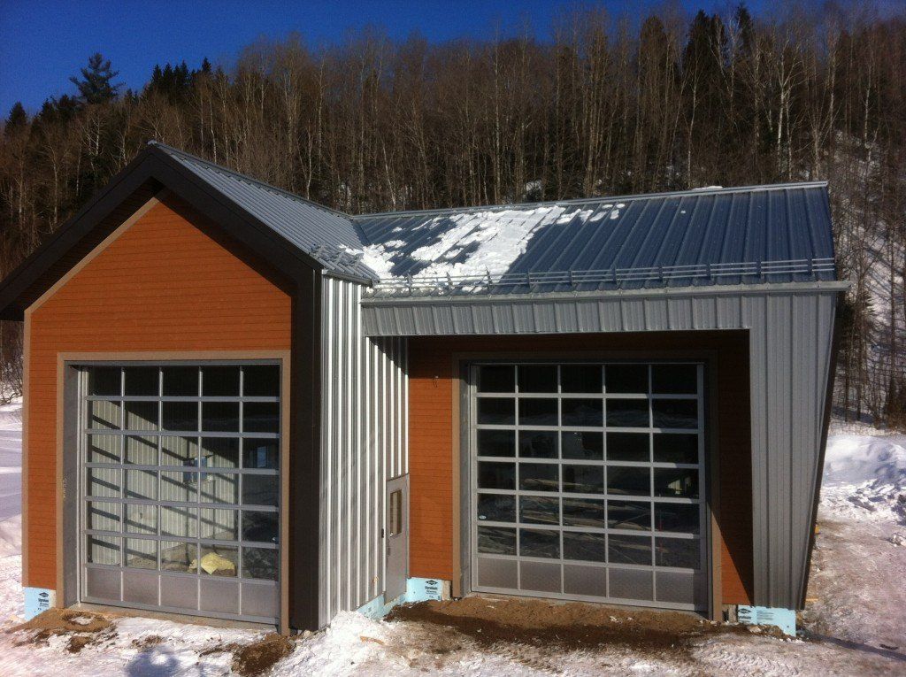 Garage avec deux portes vitrées, toit et bardage métalliques, se détachant sur un paysage enneigé et arboré.
