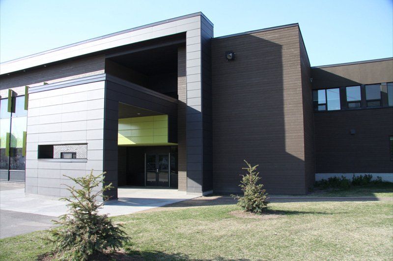 Bâtiment moderne avec façade gris foncé, grande entrée et pelouse verte.
