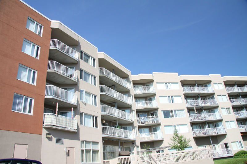 Immeuble d'appartements à plusieurs étages avec balcons, façade marron et beige, sur fond de ciel bleu.