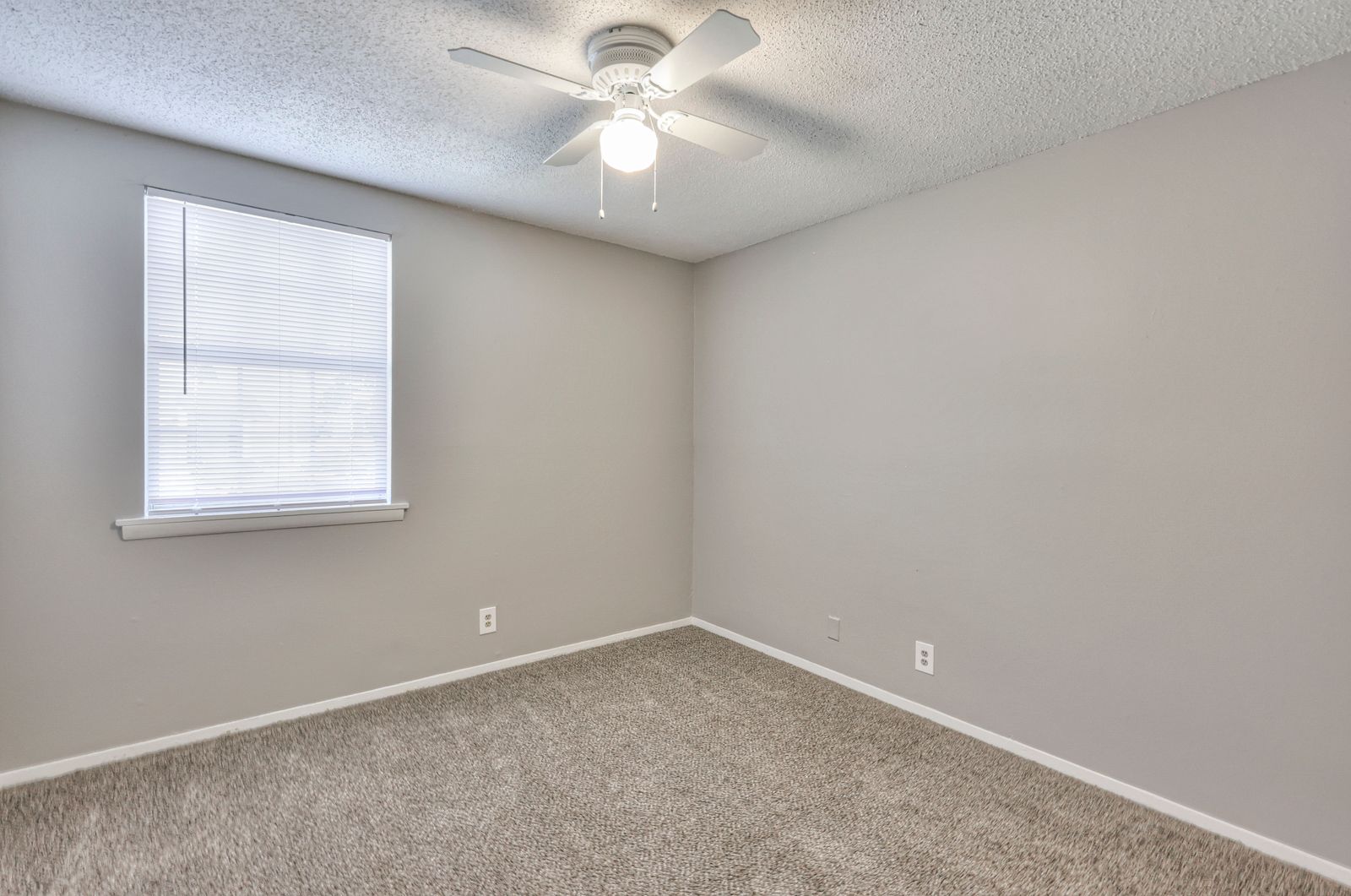 Photo of a bedroom, showing a window, carpeted flooring and a ceiling fan