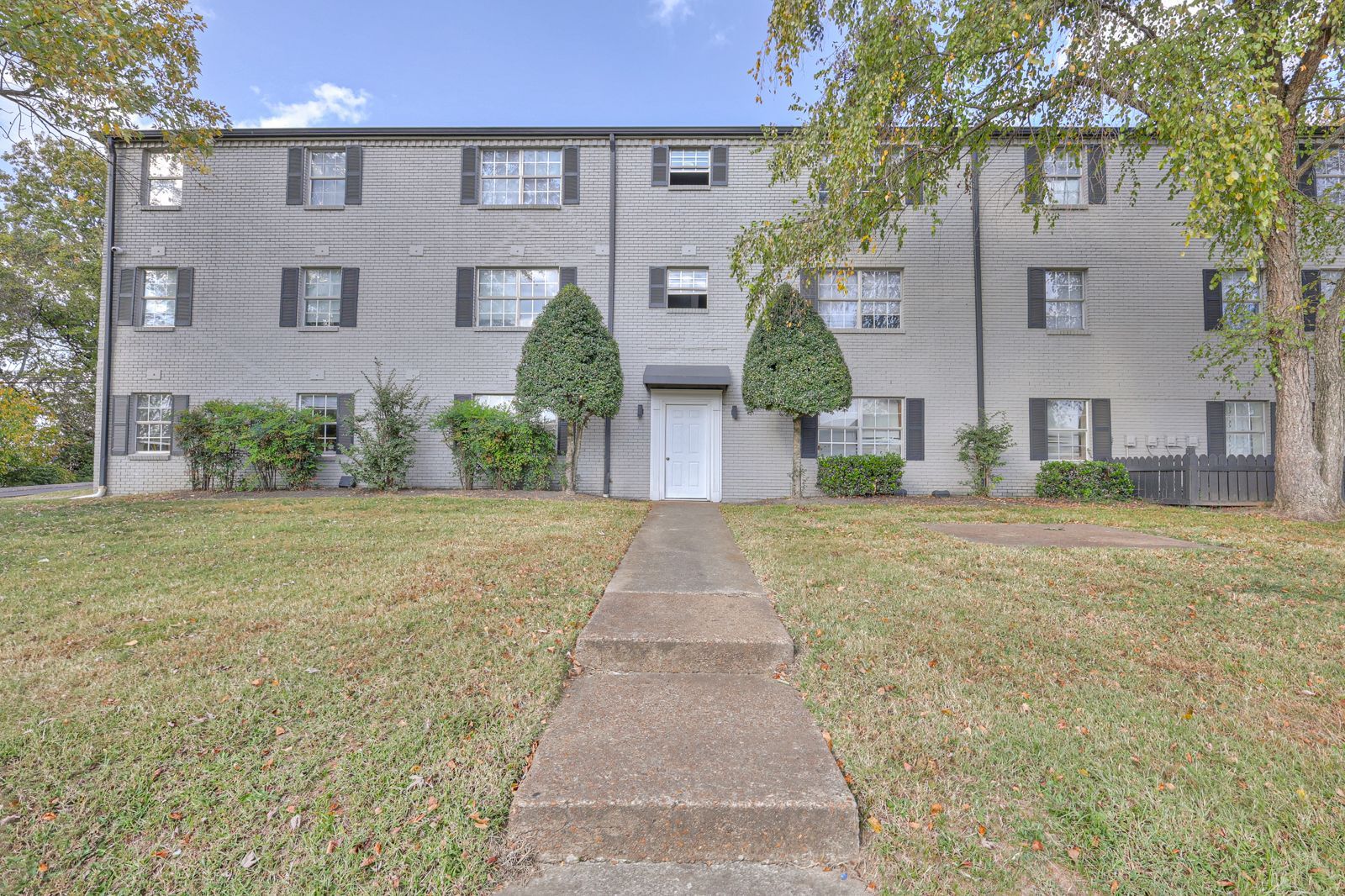 Photo of the steps leading up to a three story building, with a front door that has trees at each side