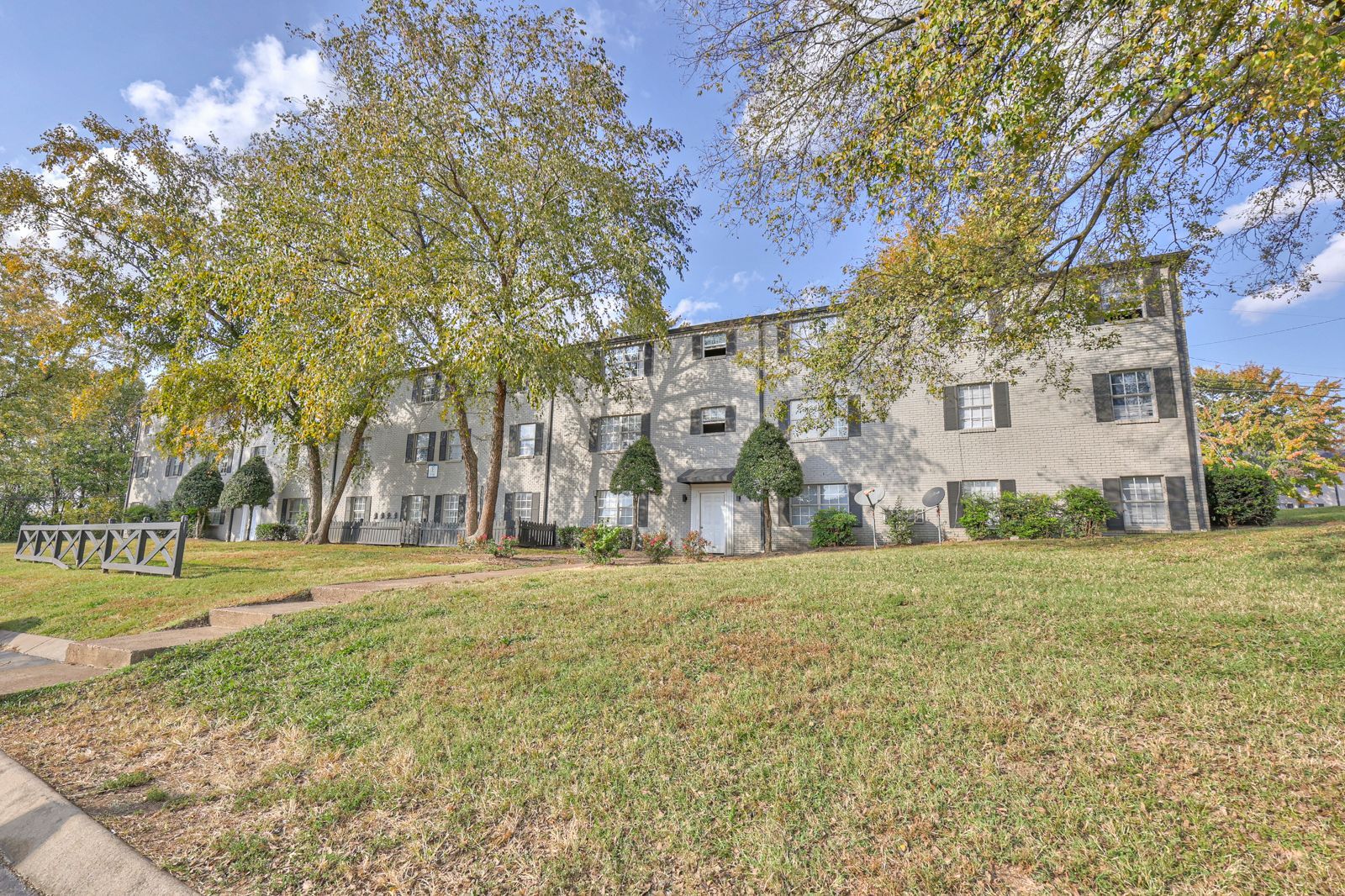Photo of a three story building, showing a grassy area out front and plenty of trees and foliage