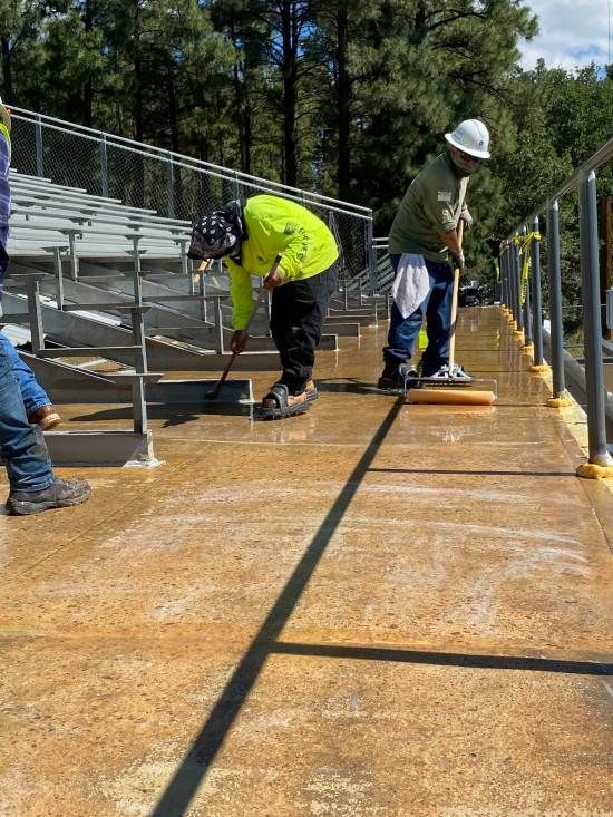 Workers cleaning a wet metal bleacher walkway on a sunny day