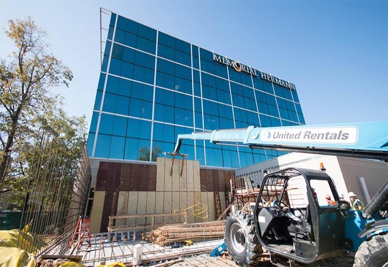 Construction site with a blue glass building facade and a United Rentals telehandler in the foreground