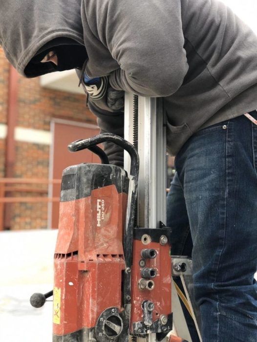 Worker using a red power drill to bore into a metal surface outdoors