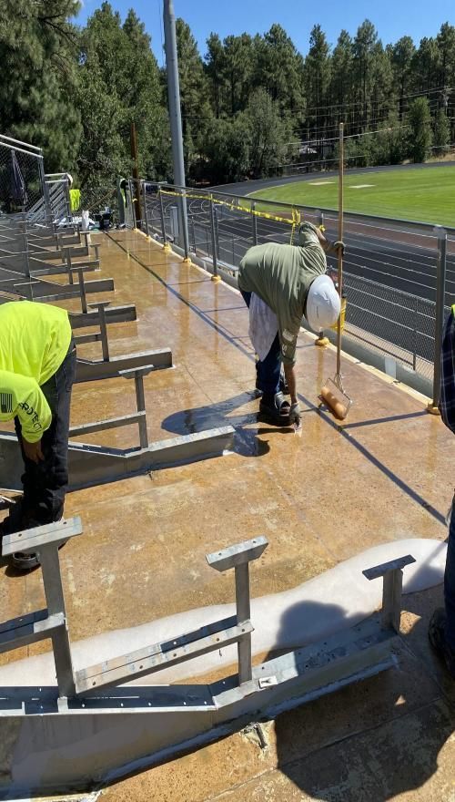 Workers coating concrete steps at an outdoor stadium seating area