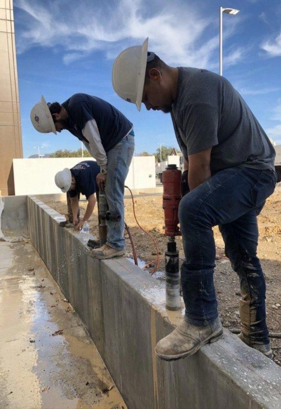 Workers in hard hats repairing a concrete wall outdoors under a blue sky