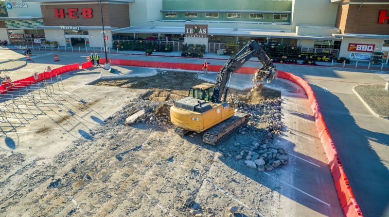 Excavator clearing rubble at a construction site beside a building with red barriers and Chinese signage