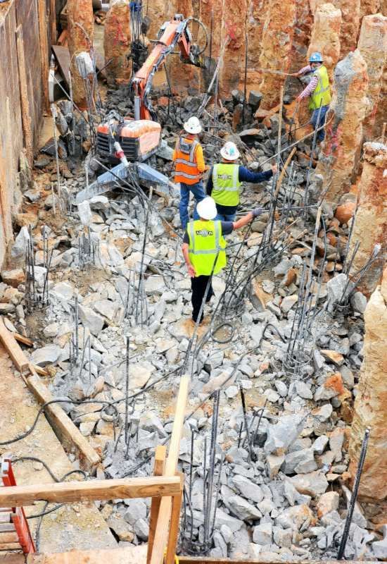 Workers in hard hats clear rubble in a rocky trench after a collapse