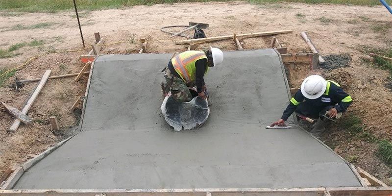 Two workers smoothing wet concrete on a large slab outdoors under construction