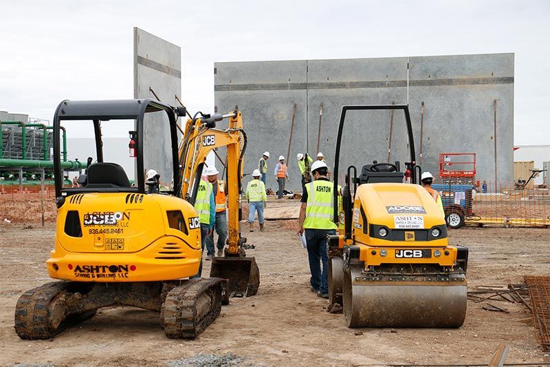 Construction crew with yellow compactors and excavator working at a building site