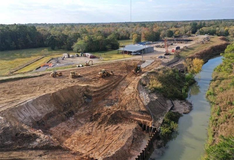 Aerial view of an active construction site beside a narrow river and wooded landscape