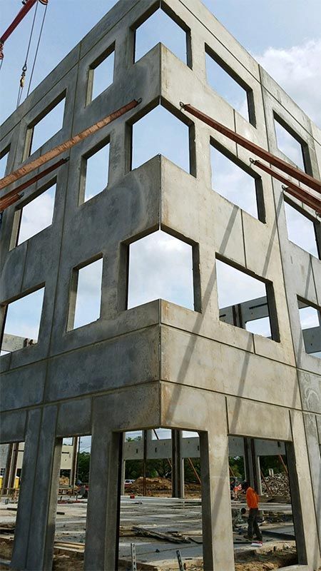 Partially built concrete structure with large window openings and a worker at the base