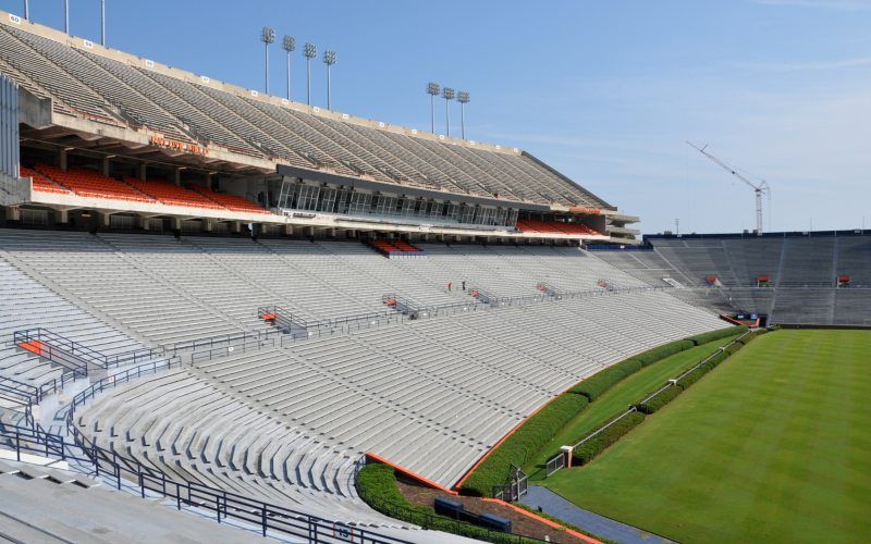 Empty stadium with gray bleachers and green field under clear daylight