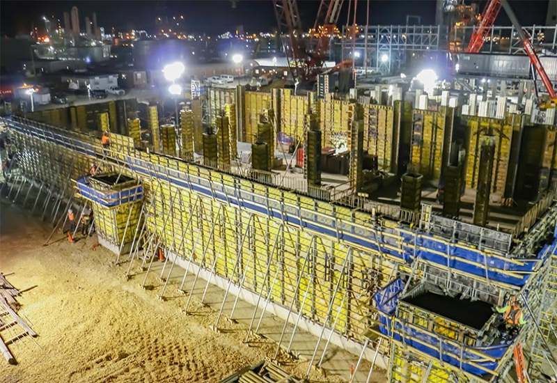 Nighttime construction site with scaffolding, cranes, and workers on a large building foundation