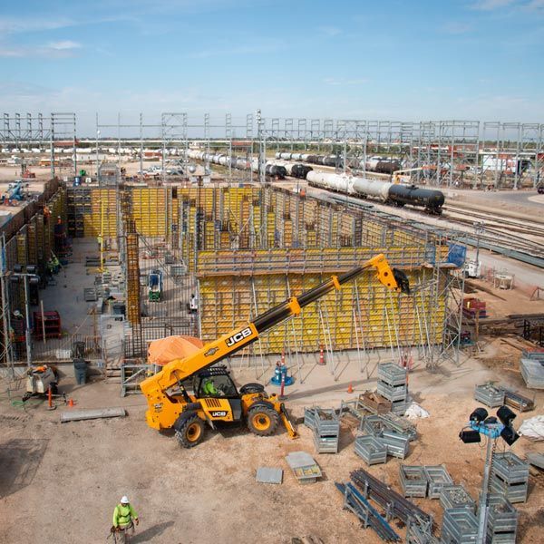 Construction site with a yellow telehandler lifting materials amid scaffolding and train tracks
