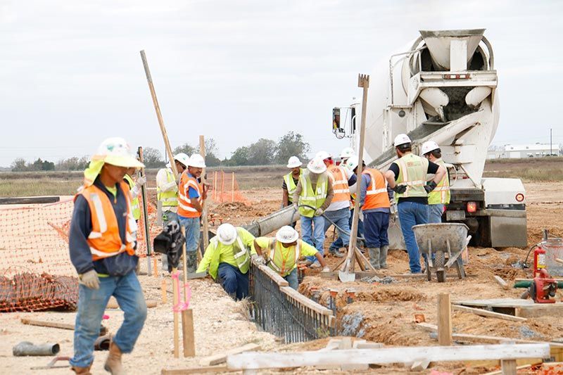 Construction crew pouring concrete at a road site beside a mixer truck