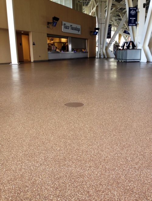 Empty indoor atrium with tan speckled floor, white columns, and a small kiosk in the background