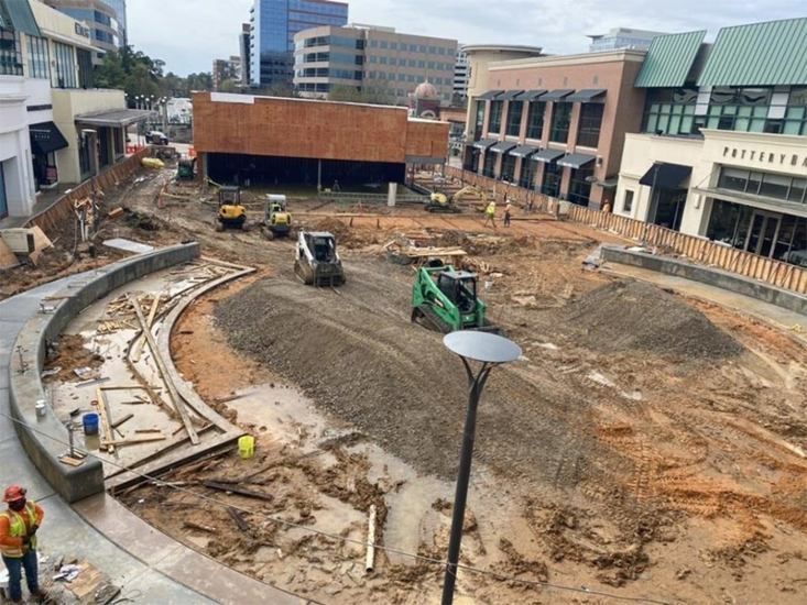 Construction site in a courtyard with excavators, dirt piles, and surrounding modern buildings