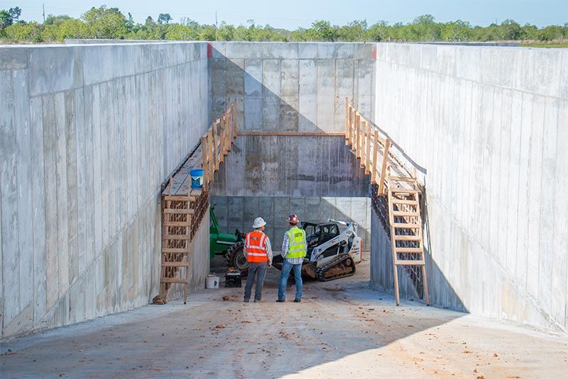 Workers inspecting a concrete construction pit with stairs and a vehicle inside