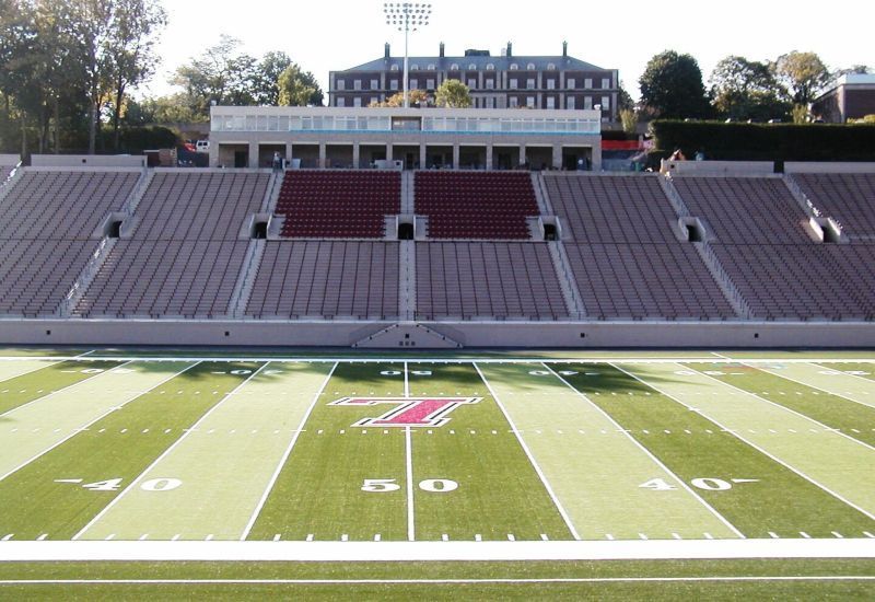 Empty football stadium with green field and red bleachers in daylight