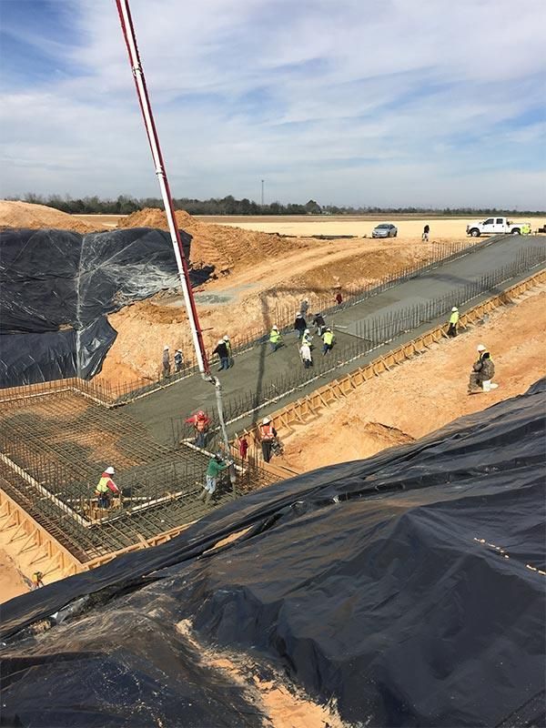 Workers building a concrete-lined canal on a construction site with black tarp and heavy machinery around them