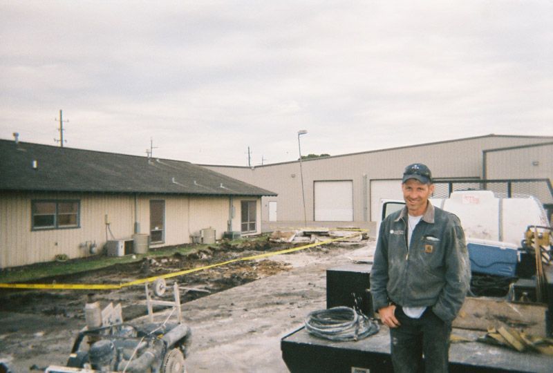 Person in work uniform standing in a damaged lot beside a building and a white truck