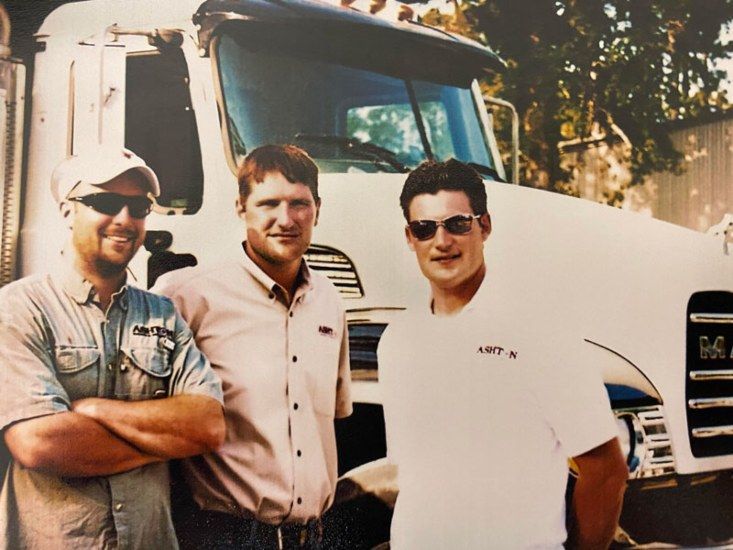 Three men standing in front of a white semi-truck, smiling outdoors.