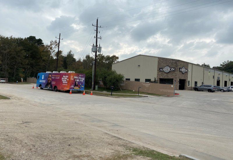 Food truck parked in an empty lot beside a beige industrial building under cloudy skies.
