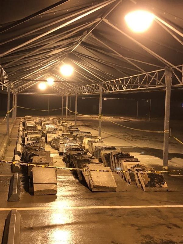 Warehouse-like shelter with rows of stacked cardboard boxes under bright lights at night