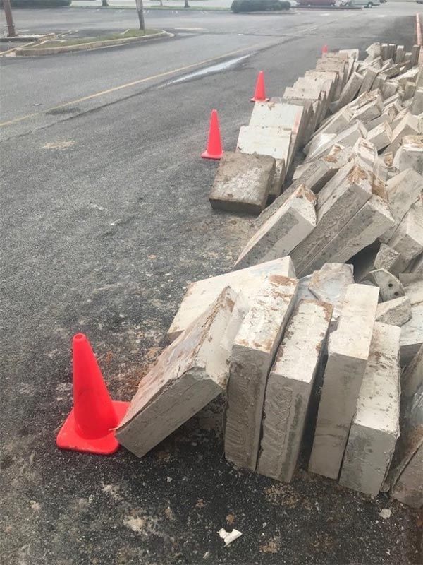 Stacked concrete blocks lined with orange cones along a roadside curb