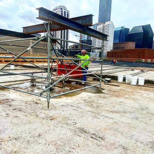 Worker in neon safety gear assembling scaffolding on a rooftop with city skyline in the background