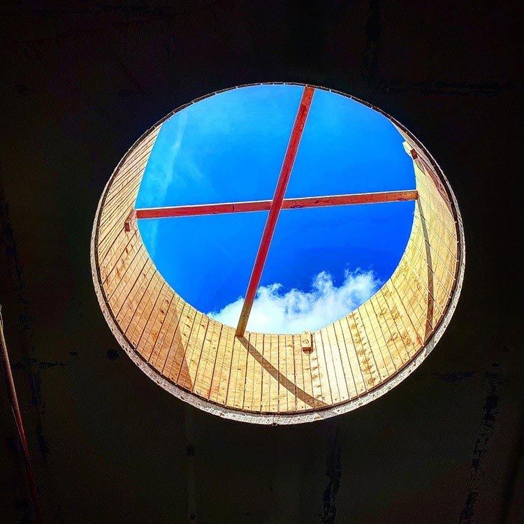 Circular skylight with red crossbars framing a bright blue sky and clouds