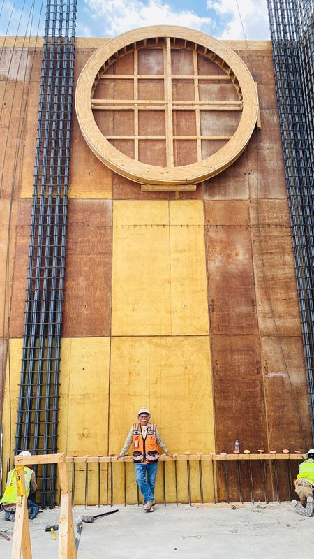 Workers standing by a large circular wall feature on a tall tan-and-brown building facade