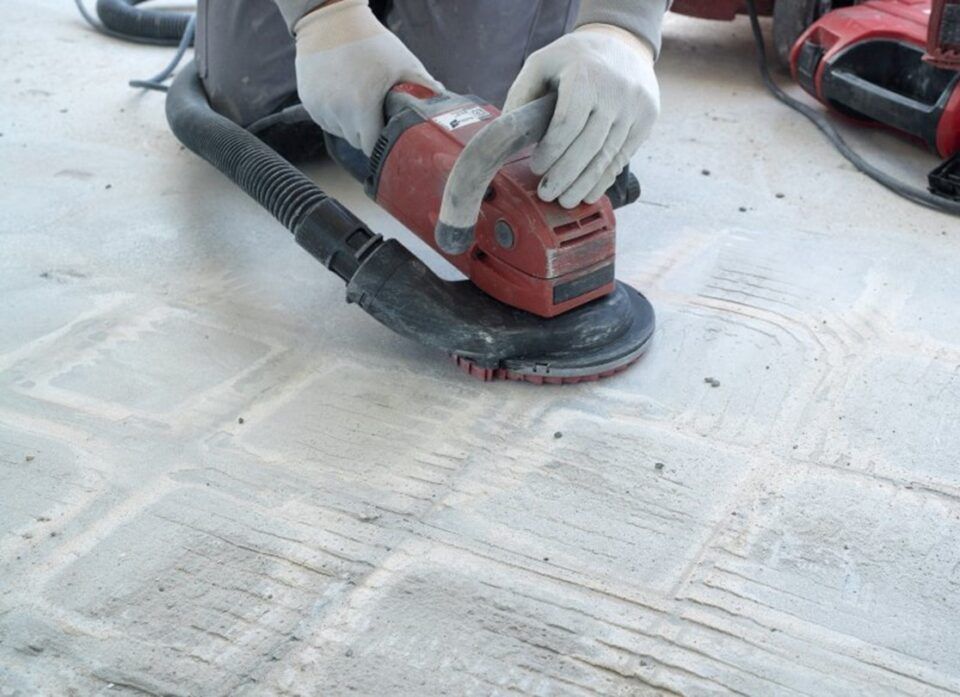 Worker sanding a concrete floor with a red floor sander and dust hose attached