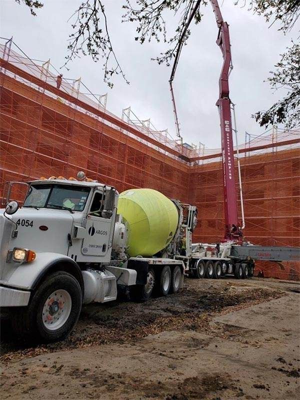Concrete mixer and pump truck at a construction site beside a brick building under construction