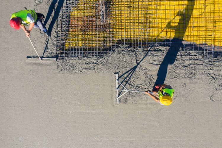 Two workers in neon vests installing a metal fence on a sandy surface, seen from above