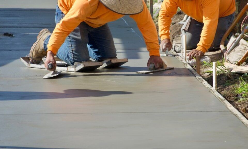 Two men in orange shirts work on a concrete sidewalk in TX and LA, focused on their task