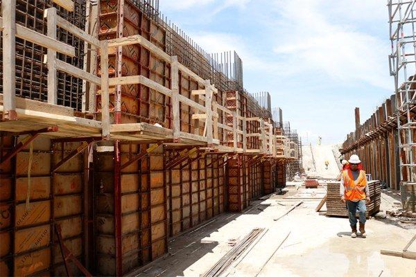Construction site with concrete forms lining both sides of a narrow path, workers in orange safety gear