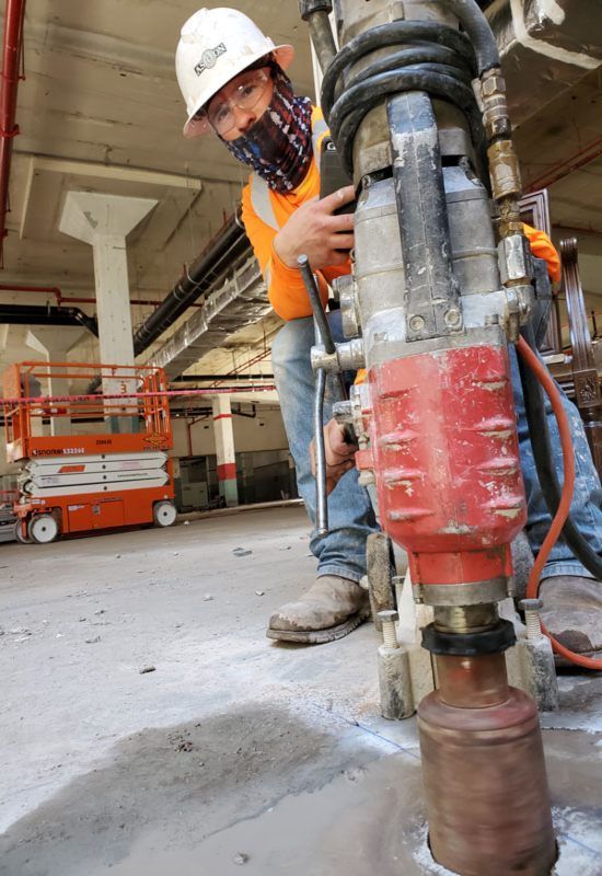 Worker in hard hat using a jackhammer on a concrete floor at a construction site