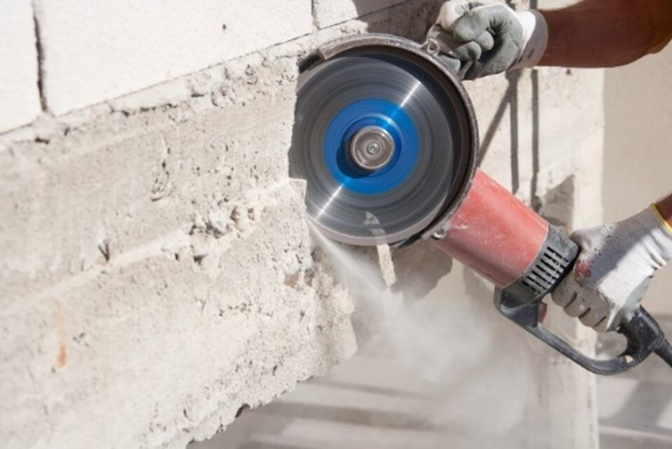 Worker using a blue concrete-cutting saw on a wall, creating dust