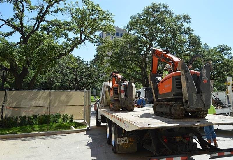 Two excavators on a flatbed truck in a tree-lined construction area