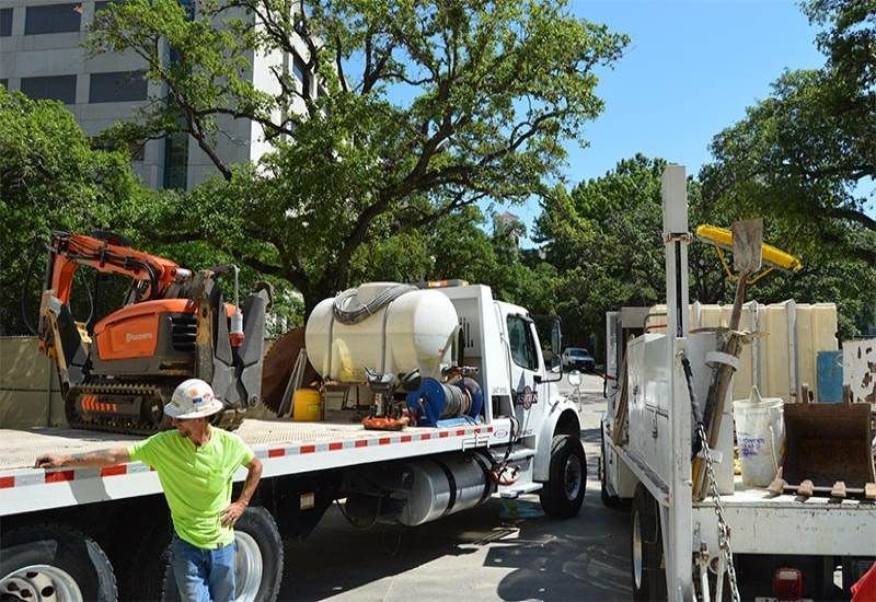 Construction crew loading equipment onto a flatbed truck on a tree-lined street