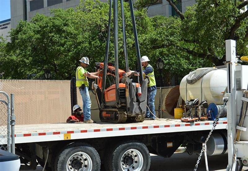 Workers loading orange machinery onto a flatbed truck at a construction site