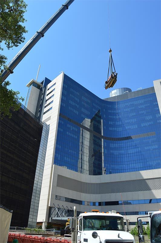 Blue glass office building with a crane lifting materials above a street-level work site