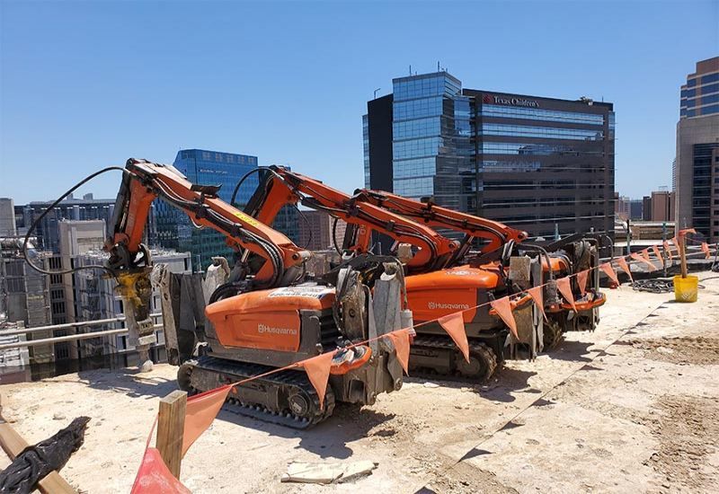 Orange excavators lined up at a construction site with tall buildings in the background