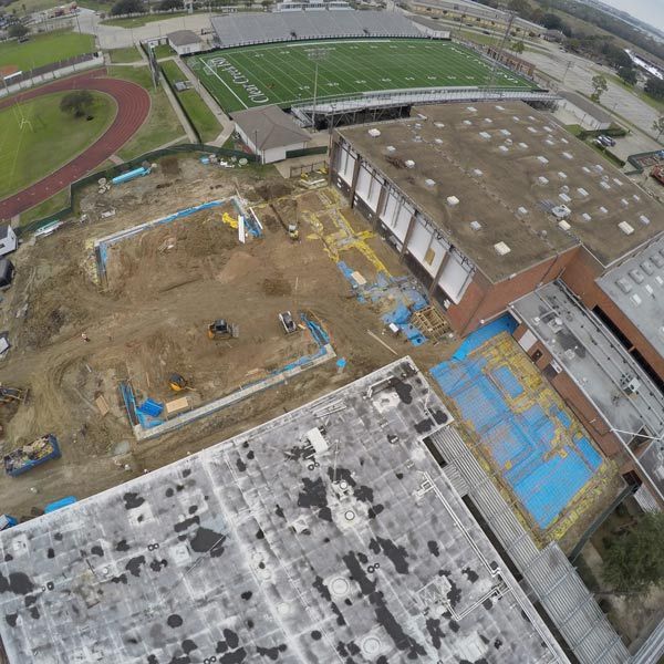 Aerial view of a construction site beside a sports field and track, with exposed soil and blue tarps.
