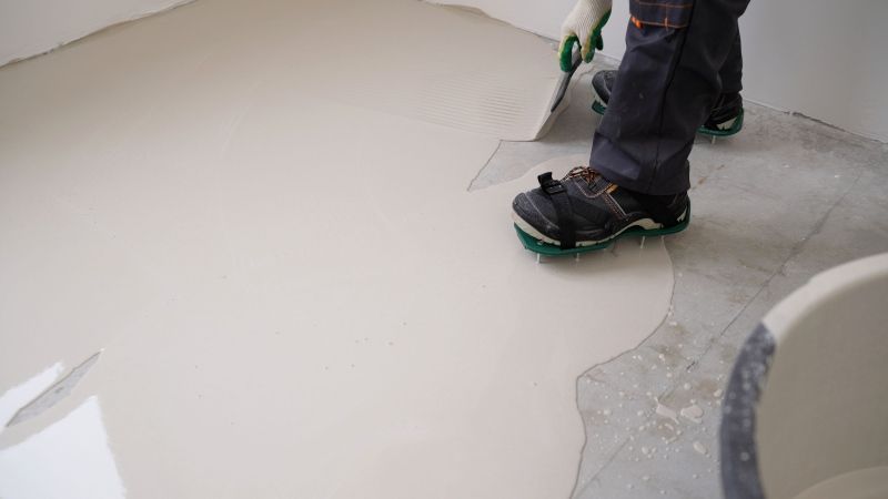 Worker standing on a smooth light-colored floor beside a curved structure, using a trowel or scraper