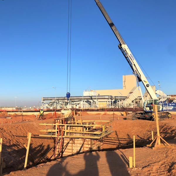 Construction site with crane lifting materials over a red dirt foundation under a clear blue sky