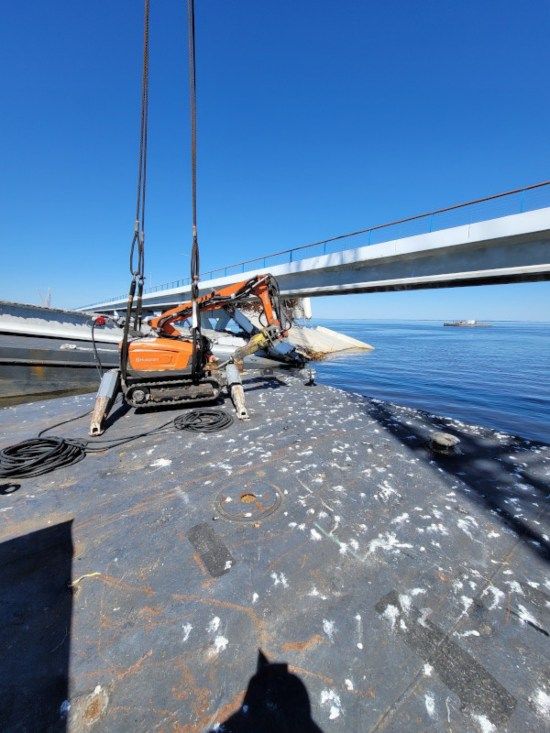 Sailboat deck with orange seat under a bridge, blue water and clear sky in the background